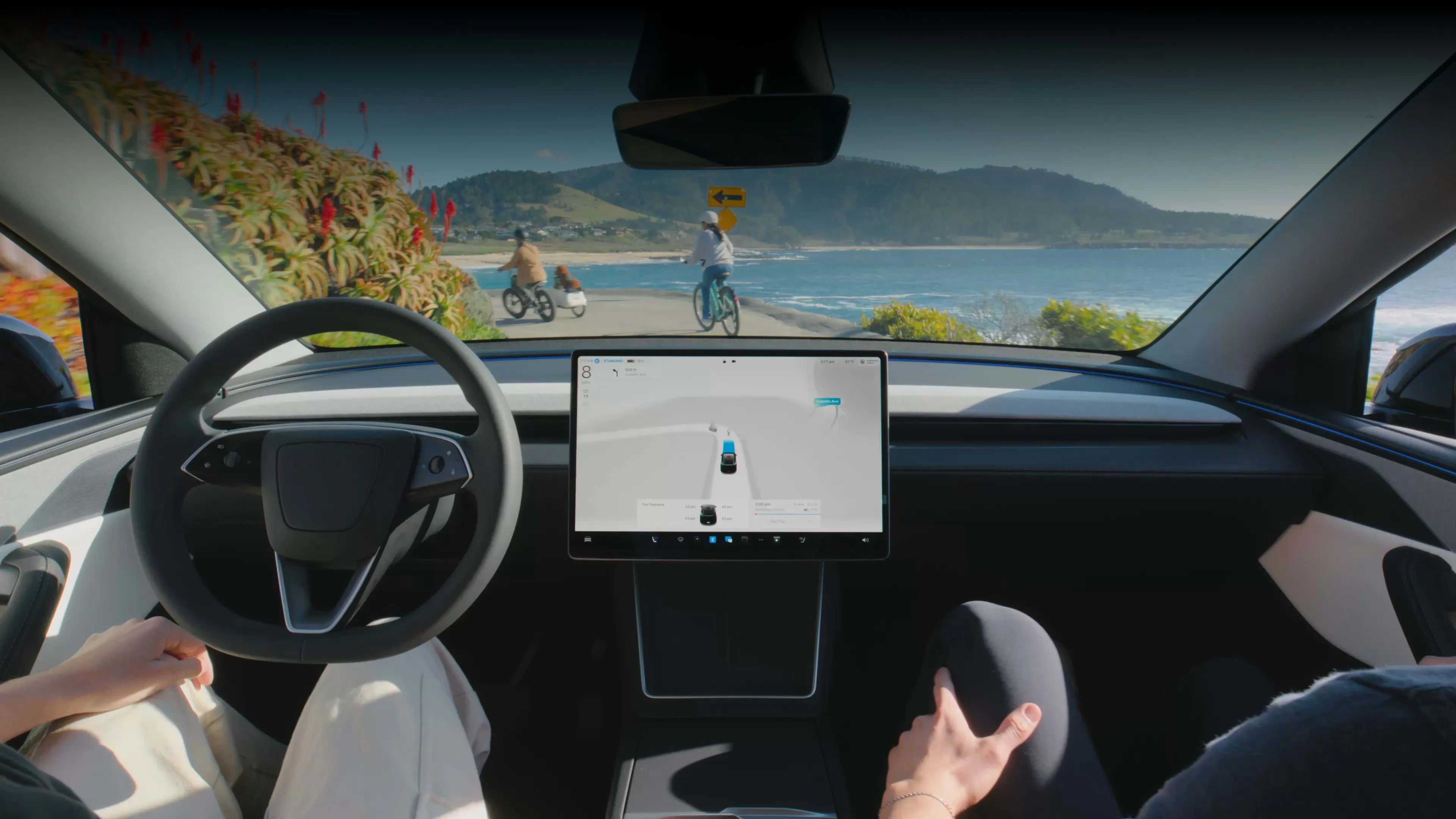 Vista interior de un Tesla con la navegación de FSD activa en la pantalla, en una carretera costera
